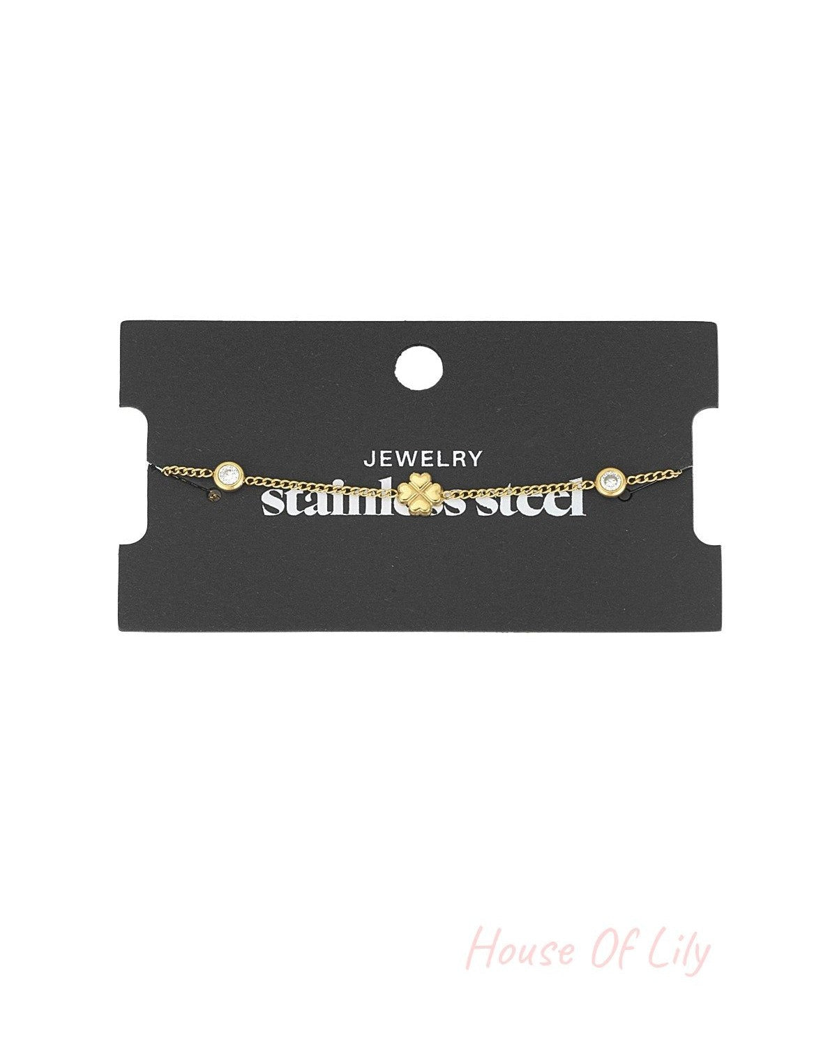 Gold four-leaf clover charm bracelet displayed on black jewellery packaging labeled stainless steel
