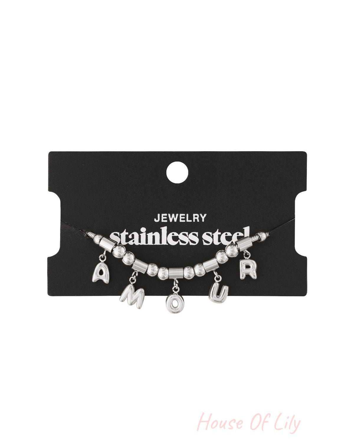 Silver stainless steel AMOUR charm bracelet displayed on black jewellery card with white writing