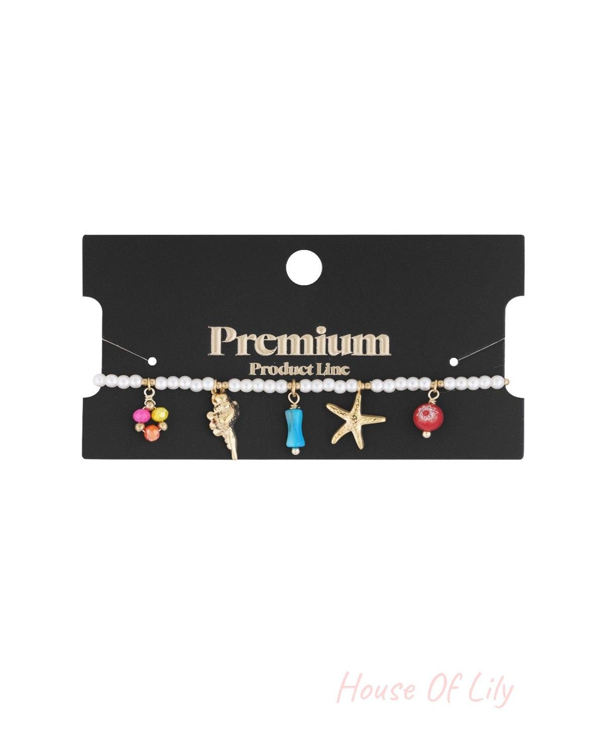 Pearl bracelet with gold ocean-themed charms displayed on premium black packaging card