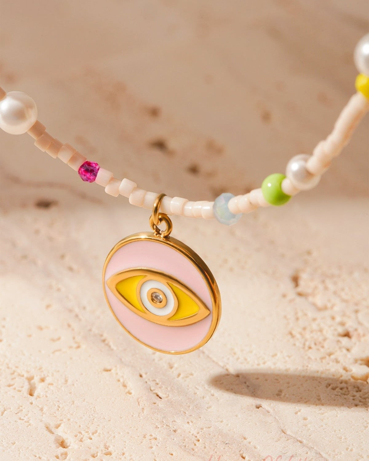 Close detailed shot of gold-tone eye charm with pastel pink and yellow enamel on beaded bracelet