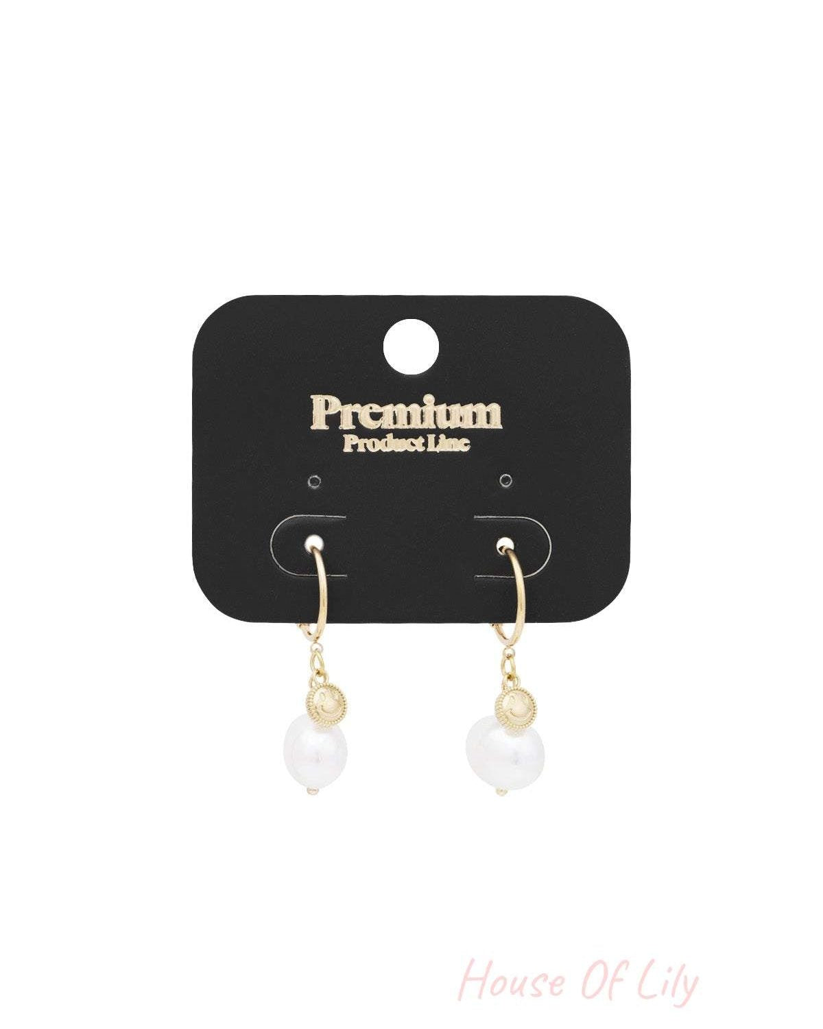 Gold-tone Happy Glow drop earrings displayed on a black premium product line card