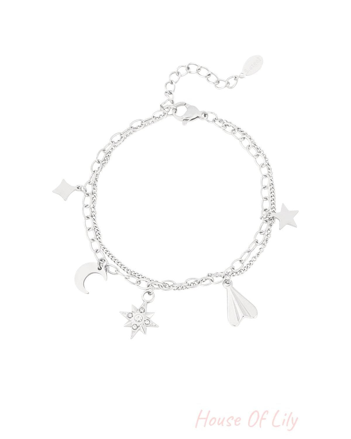 Silver-tone double chain charm bracelet with moon, star, gemstone starburst, diamond, and paper plane charms on white background