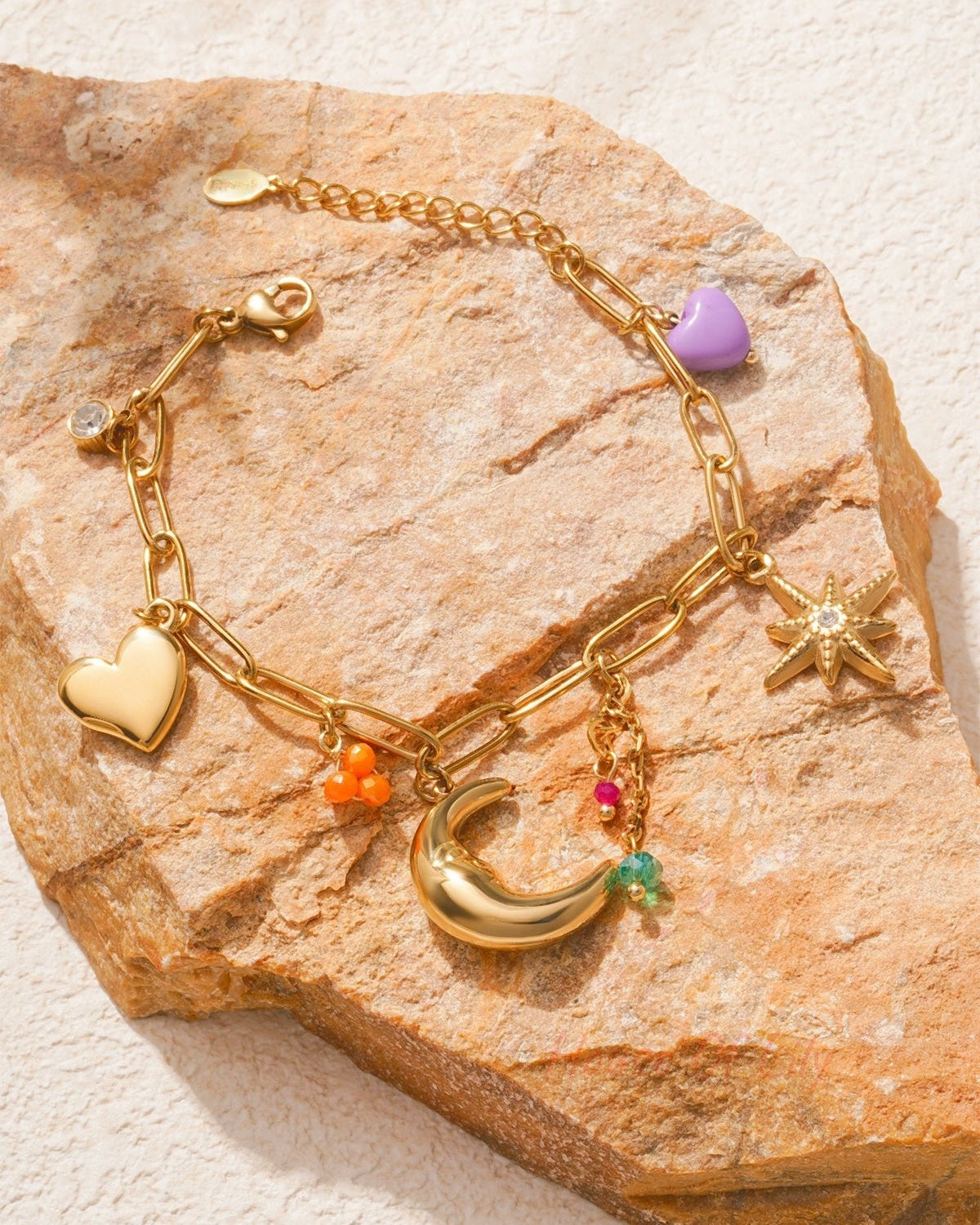 Charm bracelet artfully displayed on brown textured rock, showing detailed charms and vibrant colour contrasts