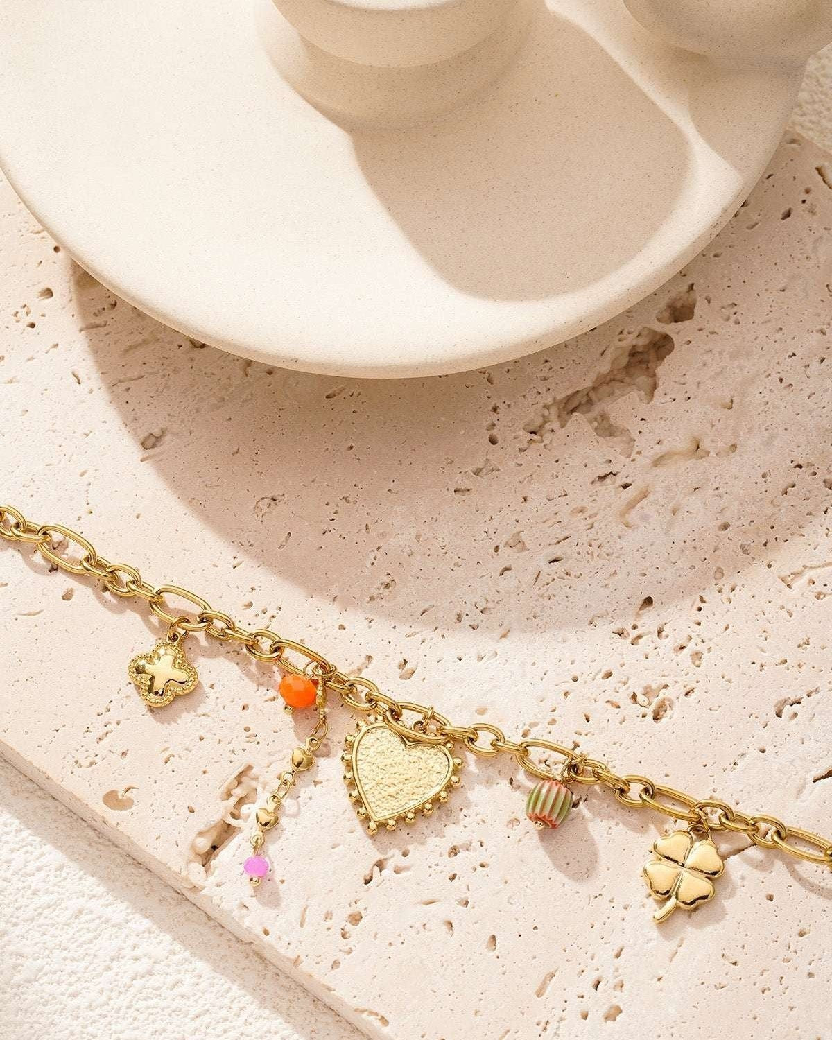 Gold charm bracelet artfully arranged on a textured beige surface with soft natural lighting