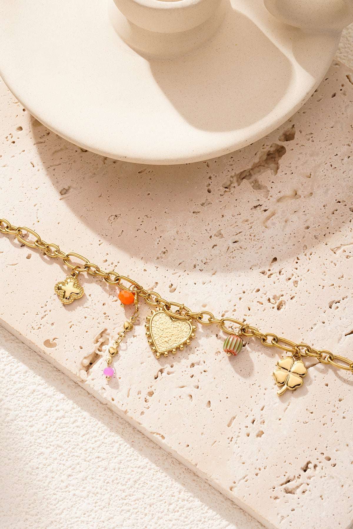Gold charm bracelet artfully arranged on a textured beige surface with soft natural lighting