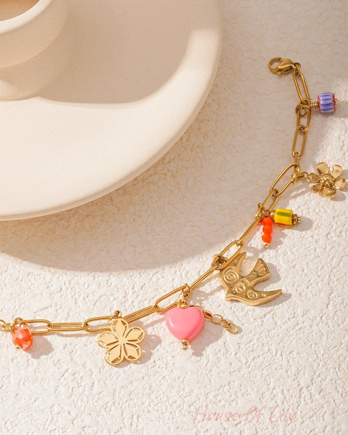 Detailed view of golden bracelet charms including pink heart, bird, and colorful beads shining in natural light
