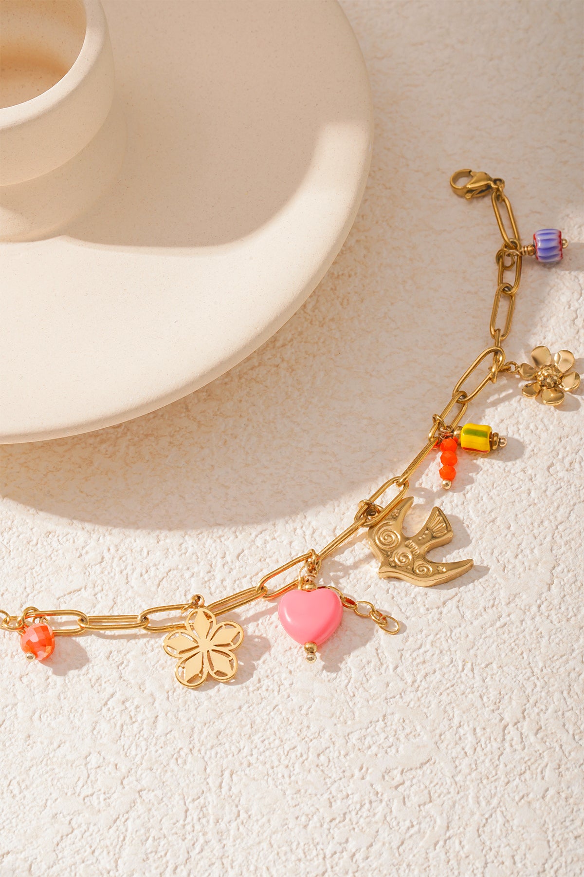 Detailed view of golden bracelet charms including pink heart, bird, and colorful beads shining in natural light