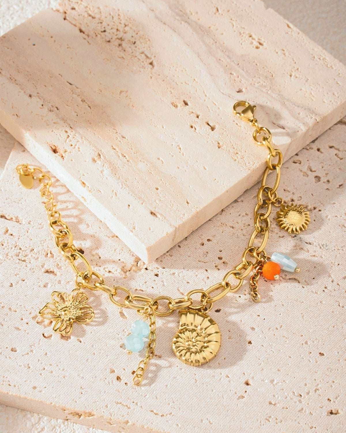 Detailed view of bracelet on textured cream stone showing gold links and ocean-themed charms with bead accents