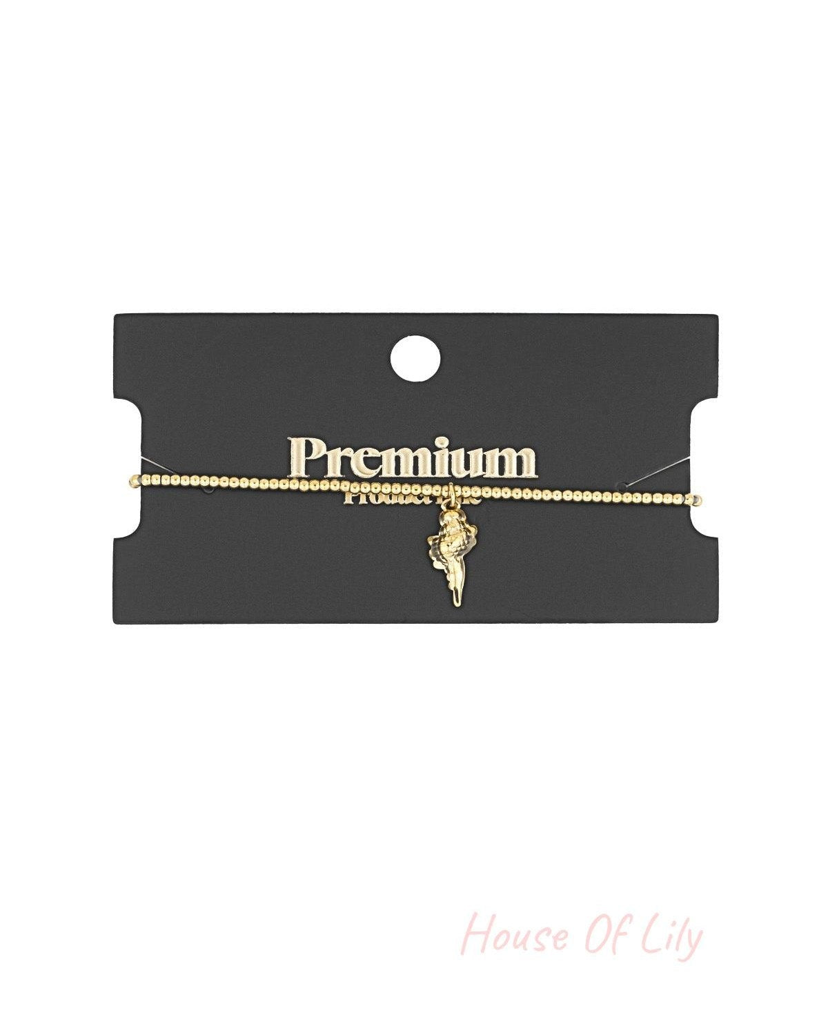 Golden beaded seashell charm bracelet displayed on a black card labeled Premium