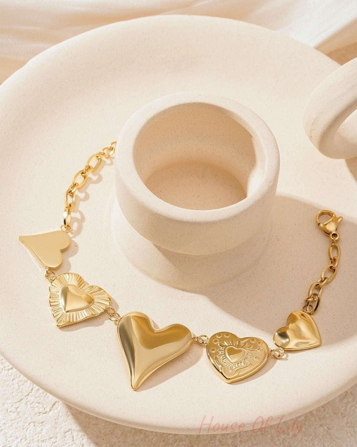 Gold chunky heart charm bracelet elegantly arranged on a cream decorative plate showing heart charms and lobster clasp