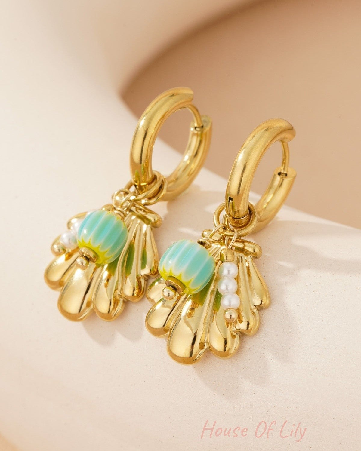 Detailed close-up of gold shell charm earrings showing turquoise enamel bead and small pearl cluster