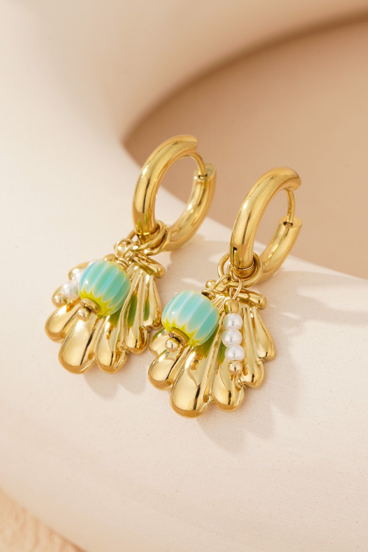 Detailed close-up of gold shell charm earrings showing turquoise enamel bead and small pearl cluster