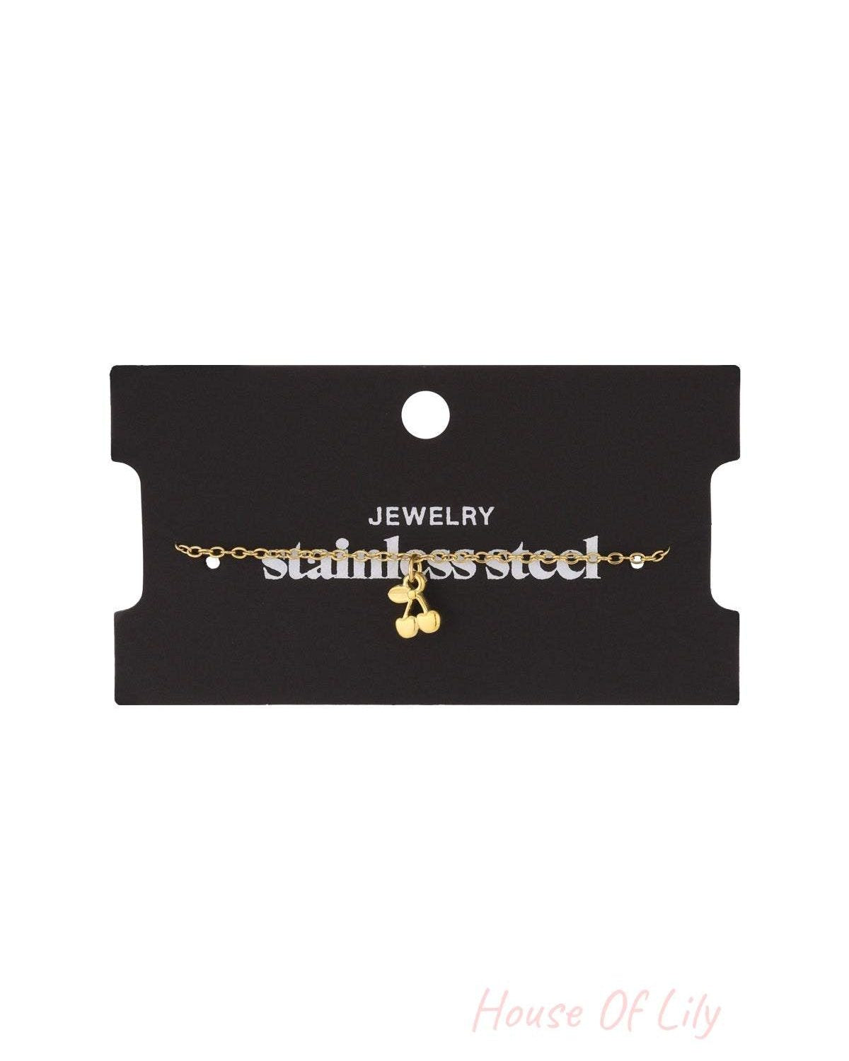Golden cherry charm bracelet displayed on a black jewelry card labelled 'stainless steel'
