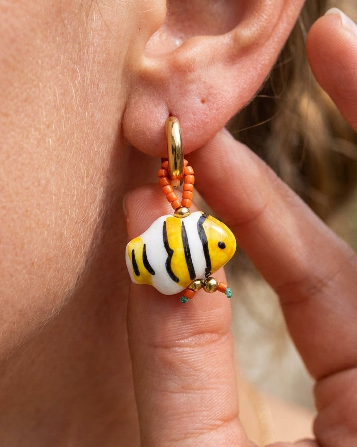 Gold hoop earring with glass fish bead, white with yellow and black stripes.