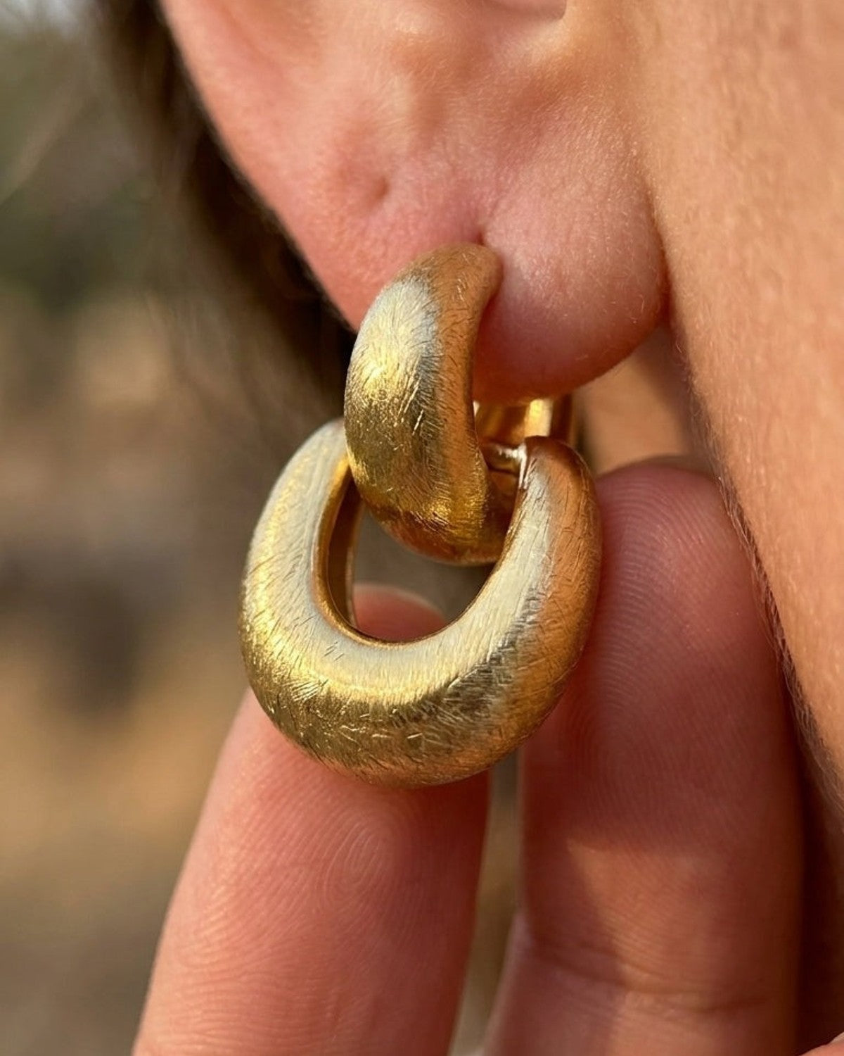 Brushed gold double-hoop drop earrings worn on an earlobe.