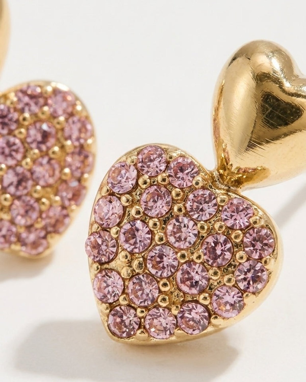 Gold stud earrings featuring a smooth heart atop a pave heart paved with pink crystals.