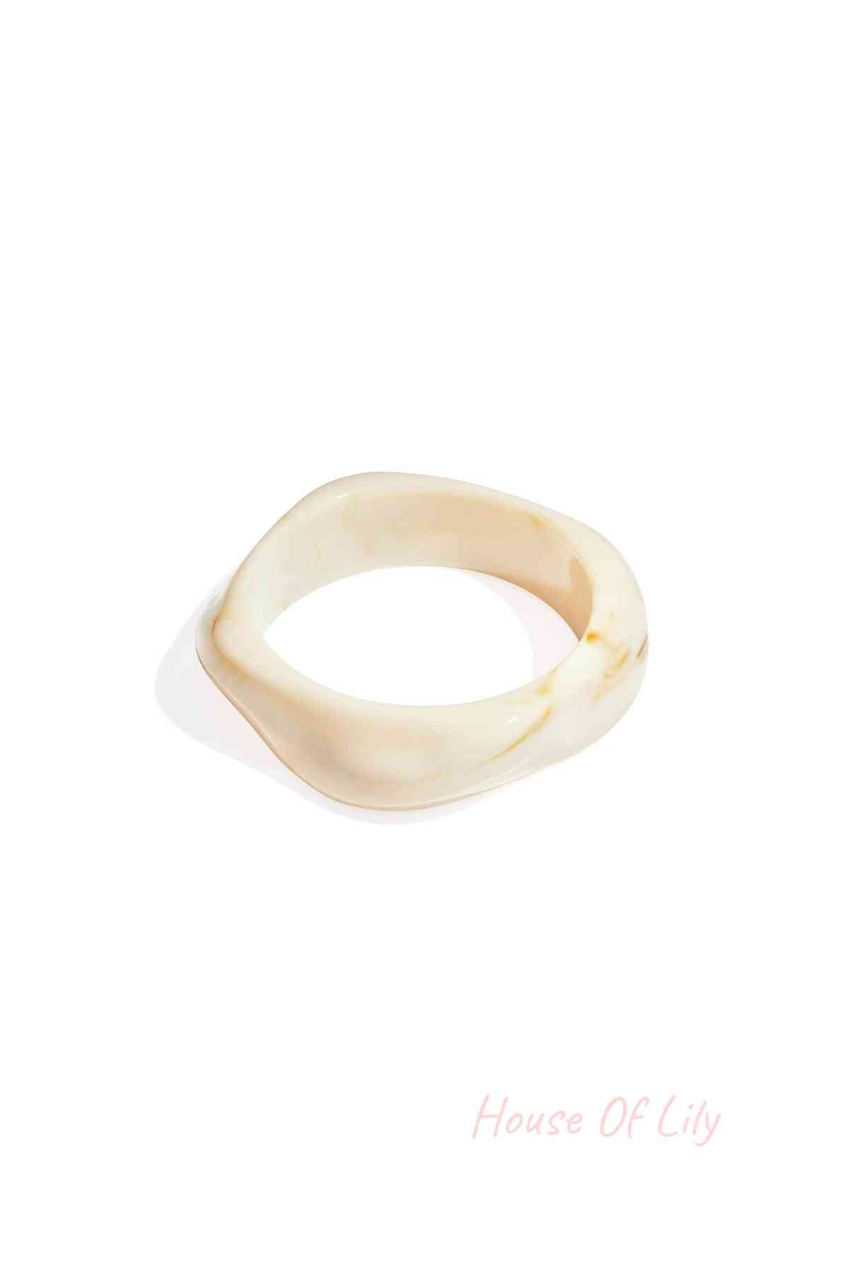 Cream-colored acrylic statement bangle with a smooth, organic, wavy shape and subtle marbled texture.