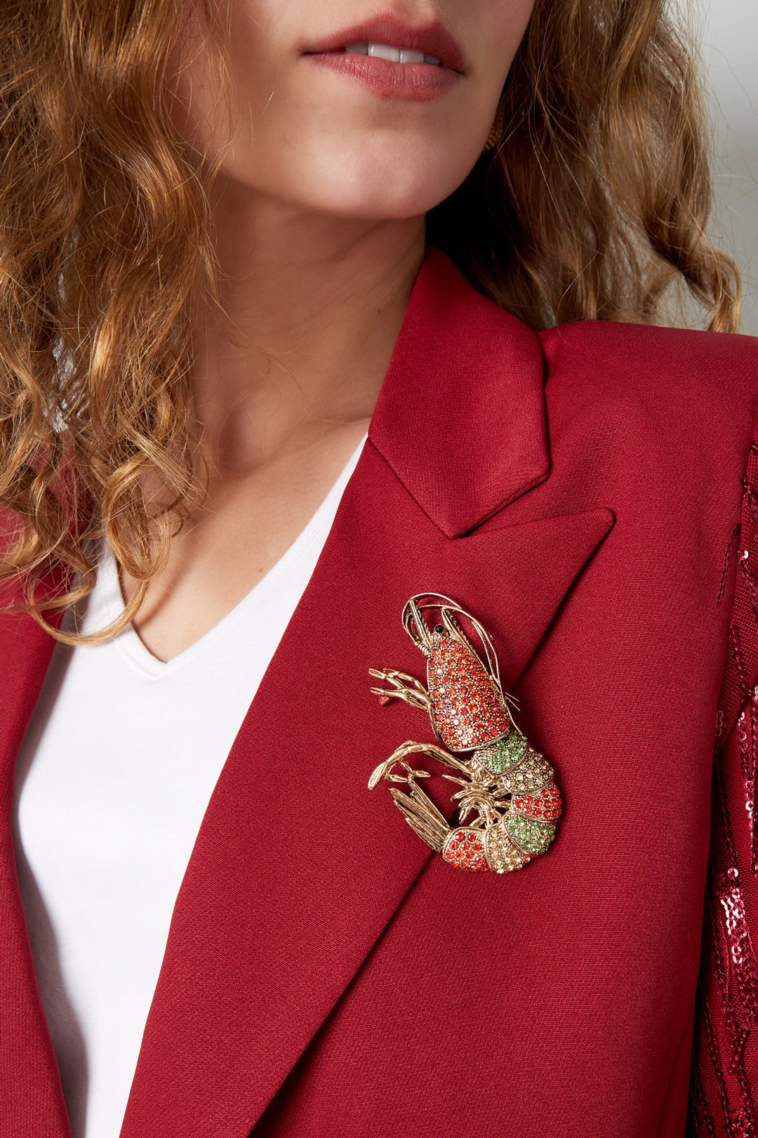 Model wearing vibrant shrimp brooch pinned on deep red blazer lapel