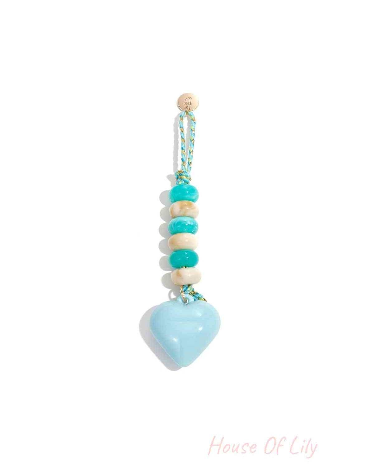 Light blue heart-shaped acrylic bag charm with alternating teal and cream beads on braided teal and gold loop hanging against white background.