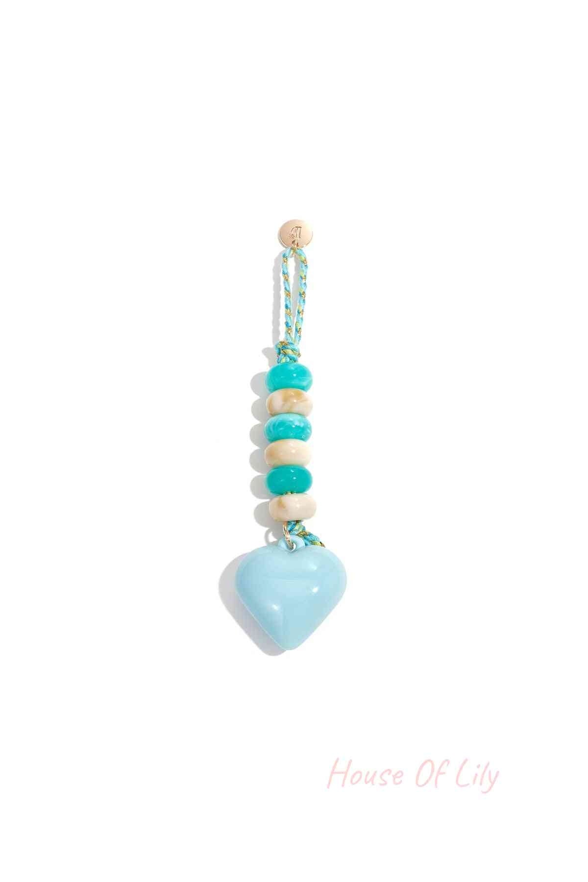 Light blue heart-shaped acrylic bag charm with alternating teal and cream beads on braided teal and gold loop hanging against white background.