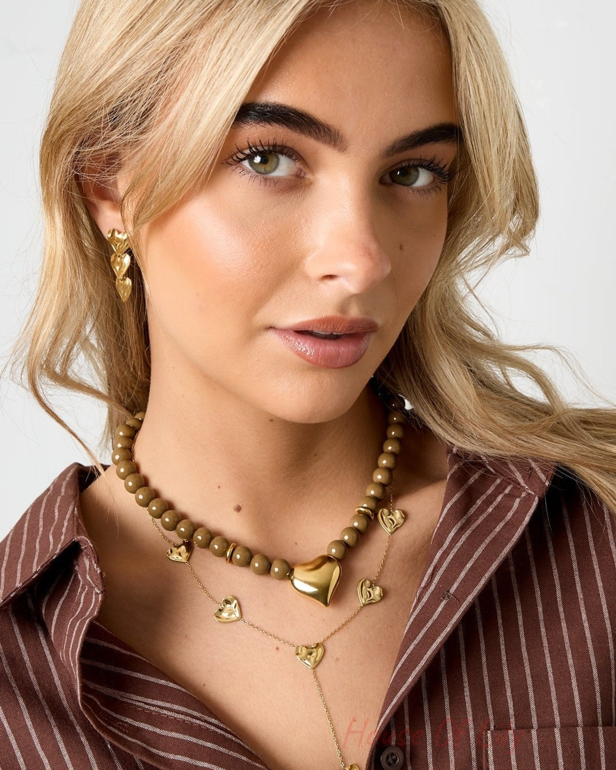 Side angle of model wearing olive bead necklace and layered necklaces with heart pendants, styled with a brown striped top