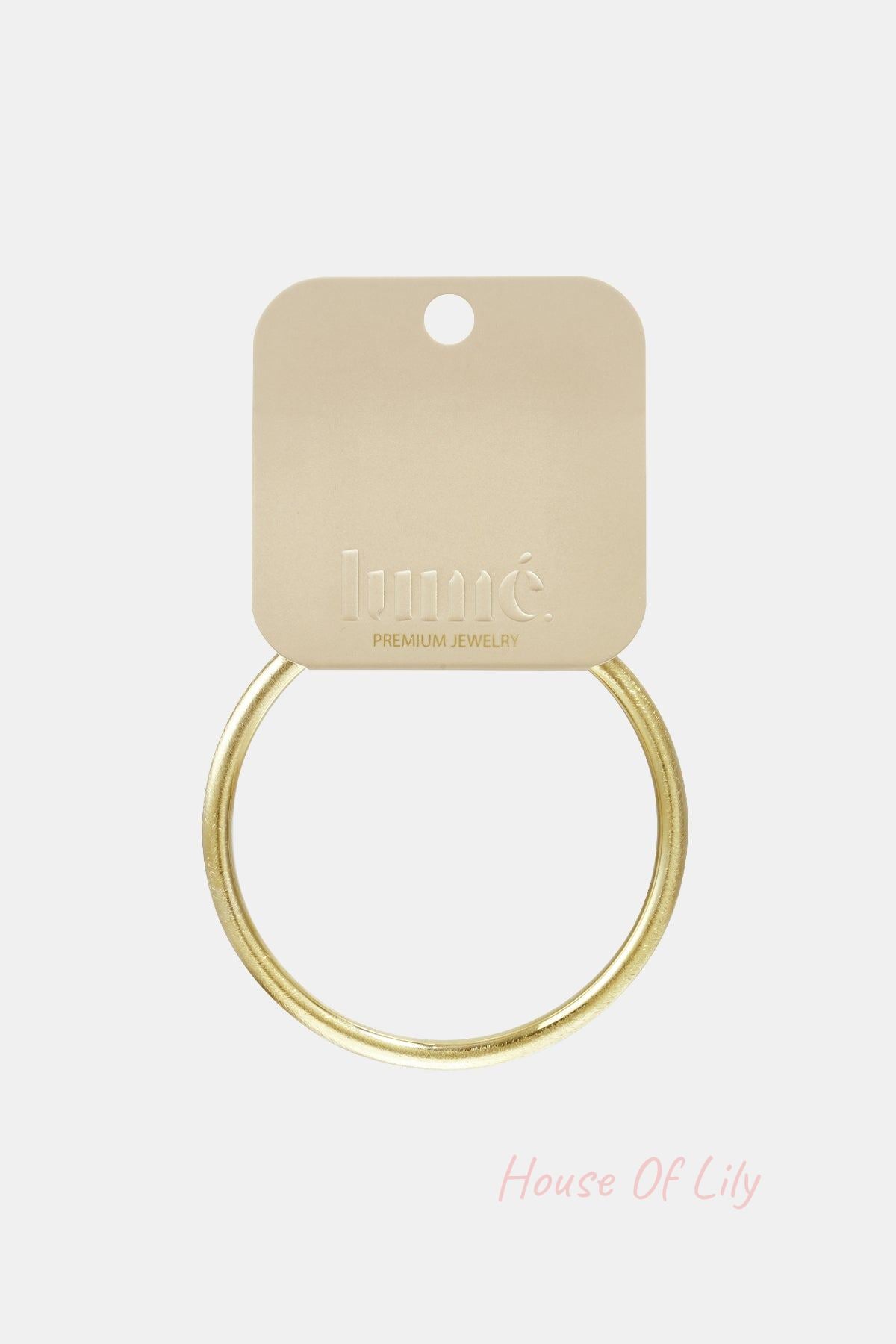 Simple gold-toned round bangle bracelet attached to a branded beige display card.