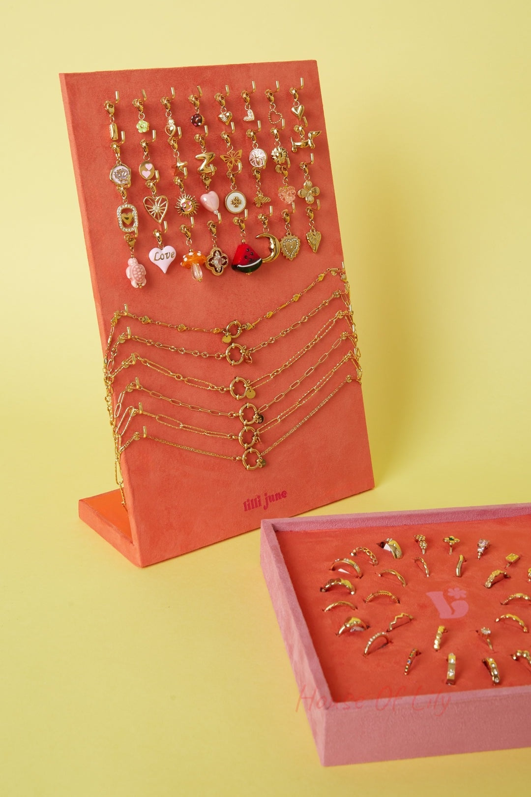 Side view of standing coral-orange velvet necklace and bracelet display alongside flat ring display with gold-tone jewelry against a yellow background