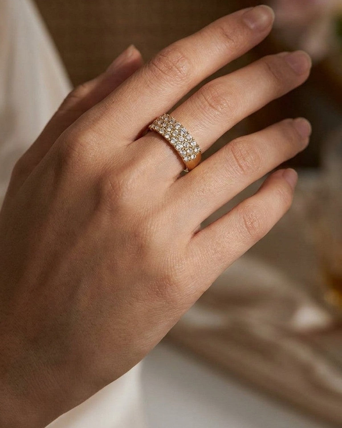 A wide gold band ring featuring three rows of pavé rhinestones, worn on a hand.