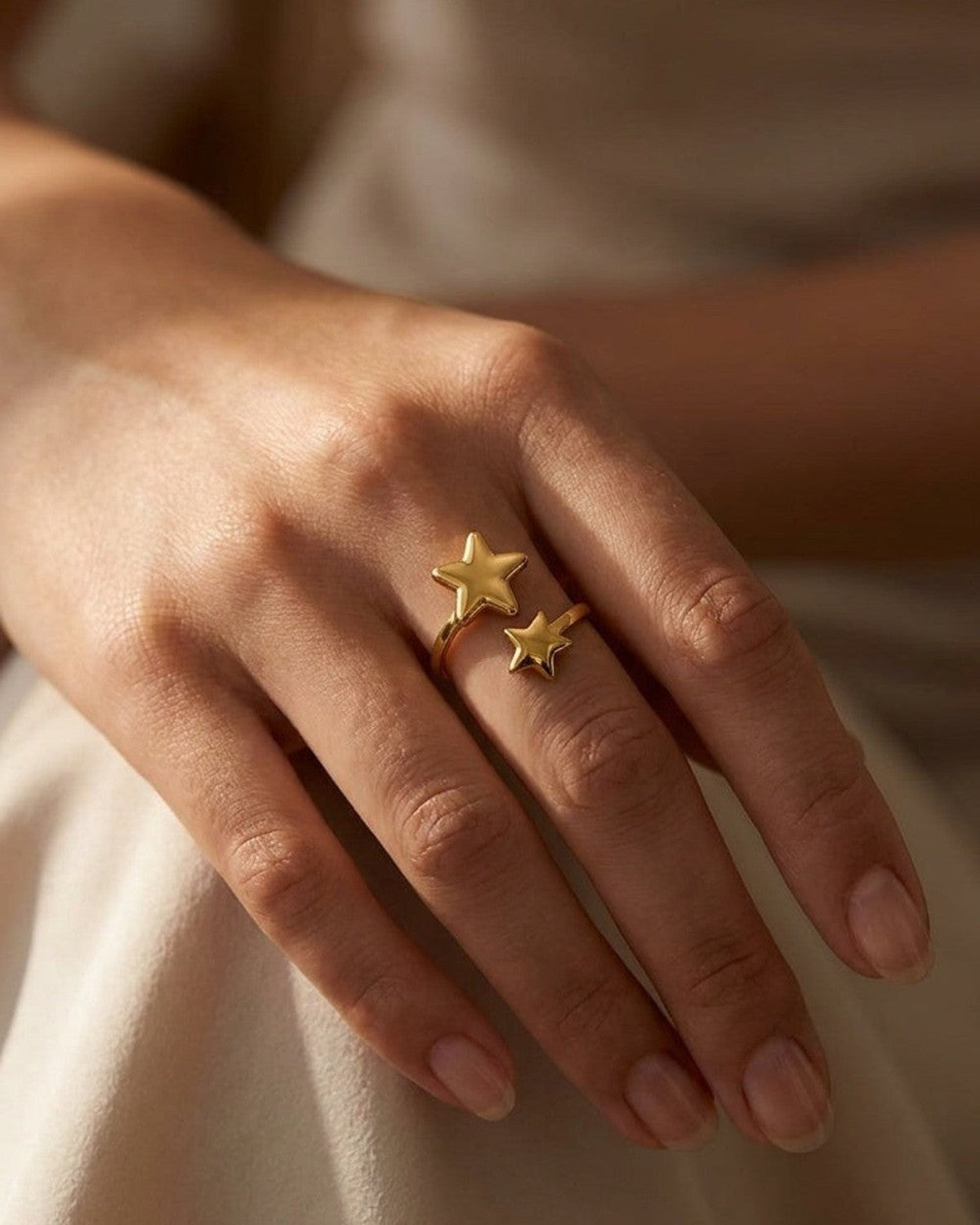 A gold minimalist ring featuring two asymmetrical star motifs on an open band, worn on a hand.