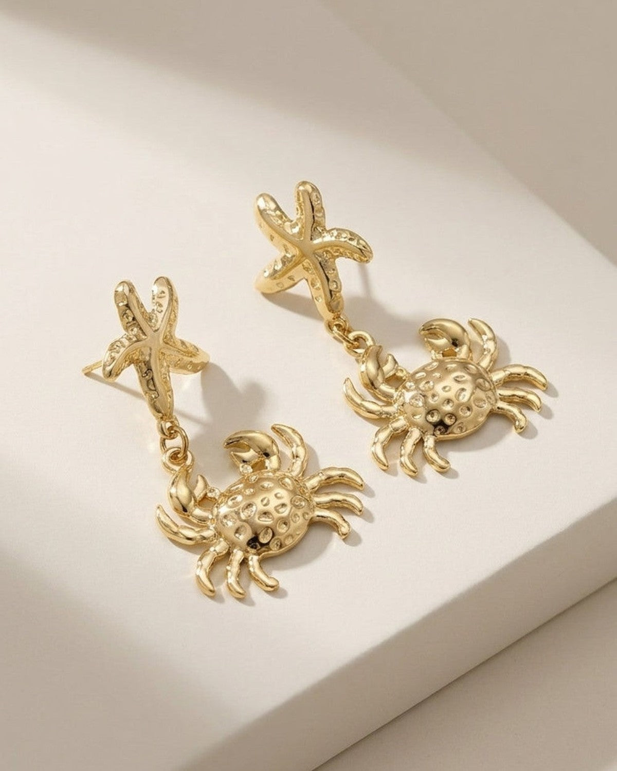 Gold drop earrings featuring a starfish stud dangling a textured crab pendant.