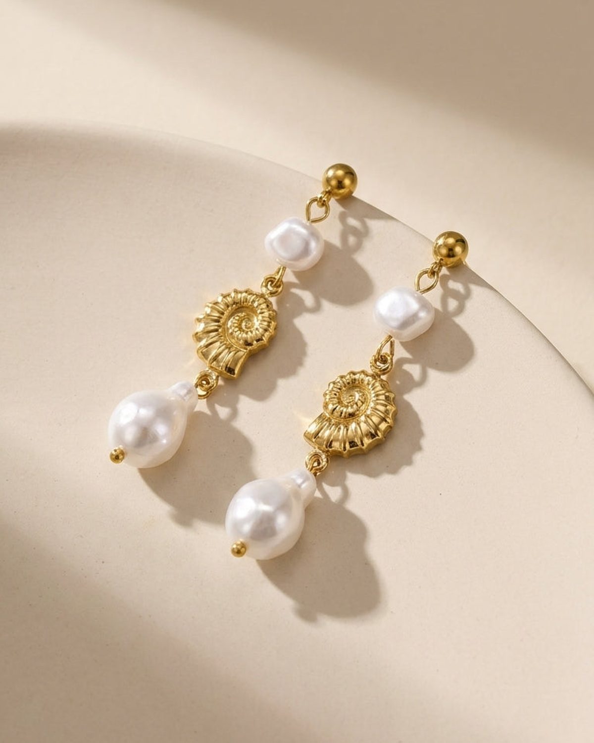 Gold drop dangle earrings featuring white pearls and textured shell charms.