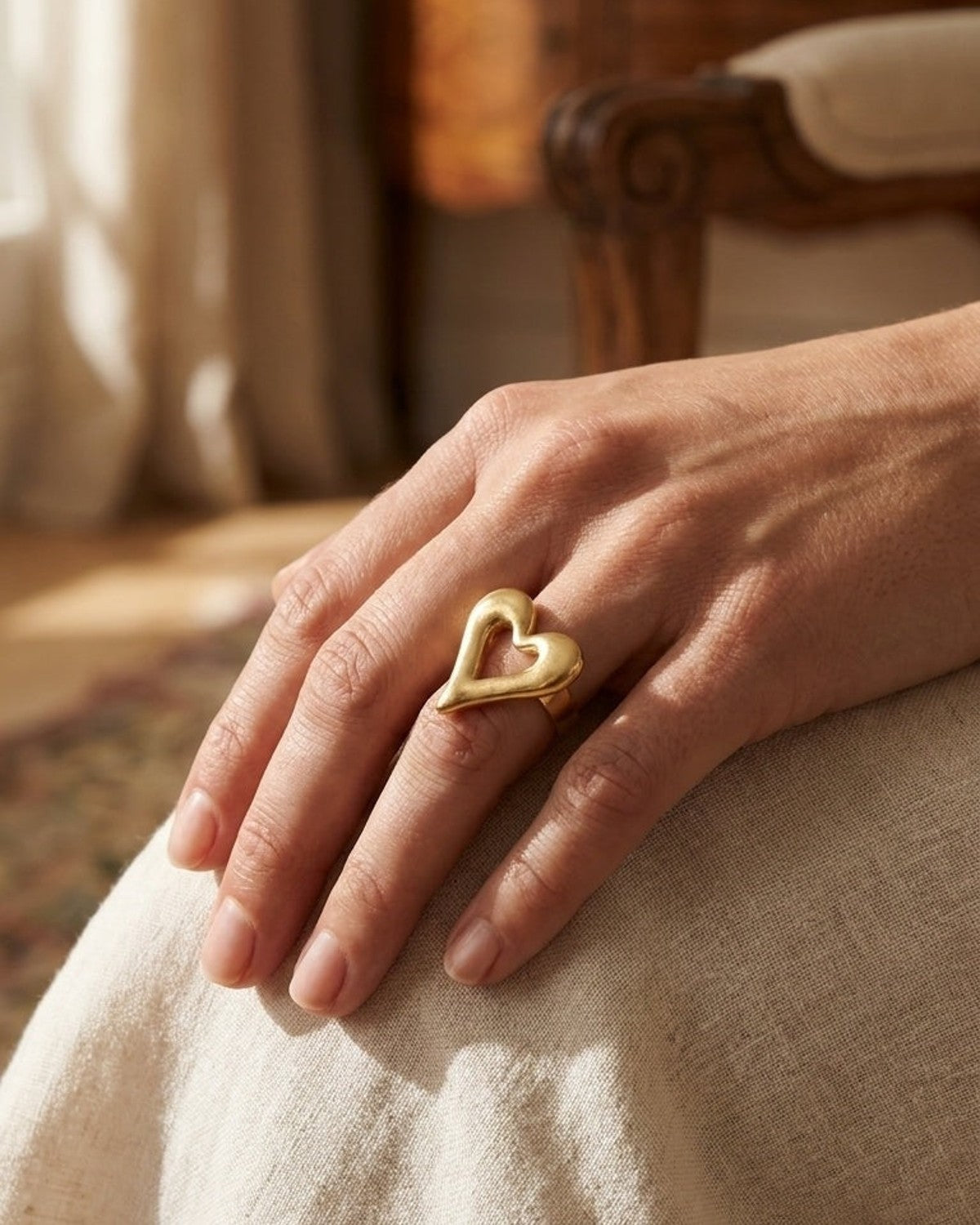 A chunky gold-toned metal ring with an open heart design worn on a person's finger.