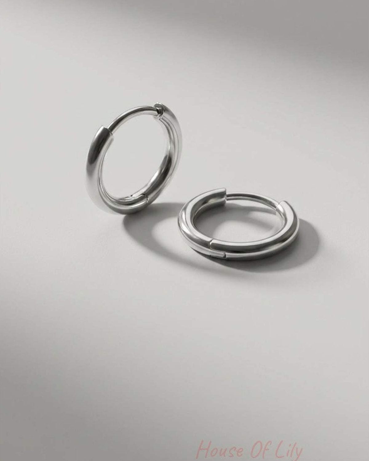 Minimalist silver huggie hoop earrings with a smooth, polished finish on a light grey background.