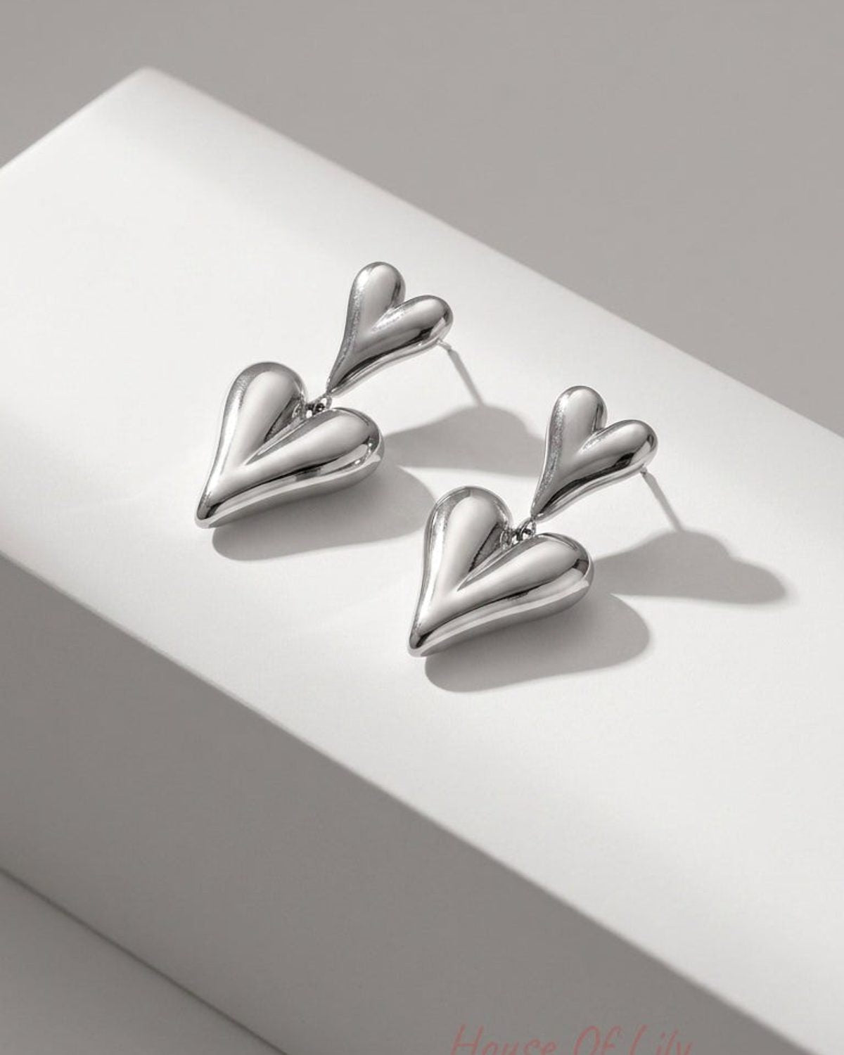 Polished silver drop earrings featuring two connected puffed heart charms on a white display block.