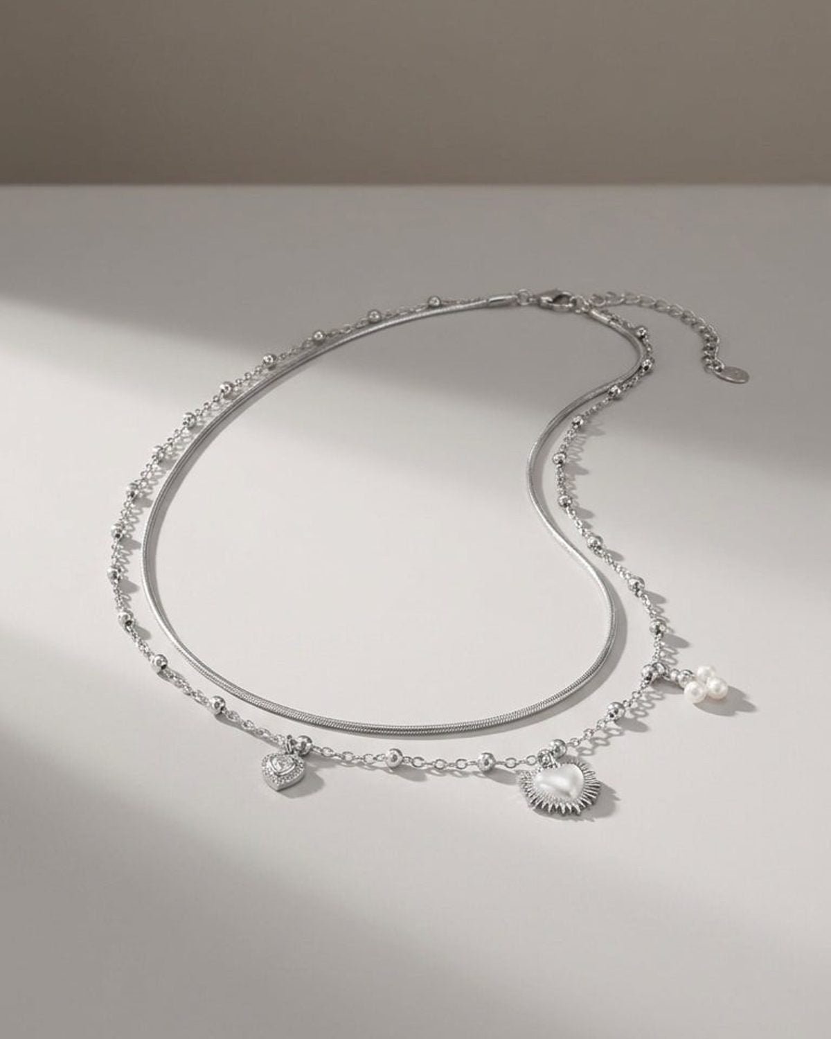 Silver layered coquette necklace with heart charms and pearl accents on a light surface.