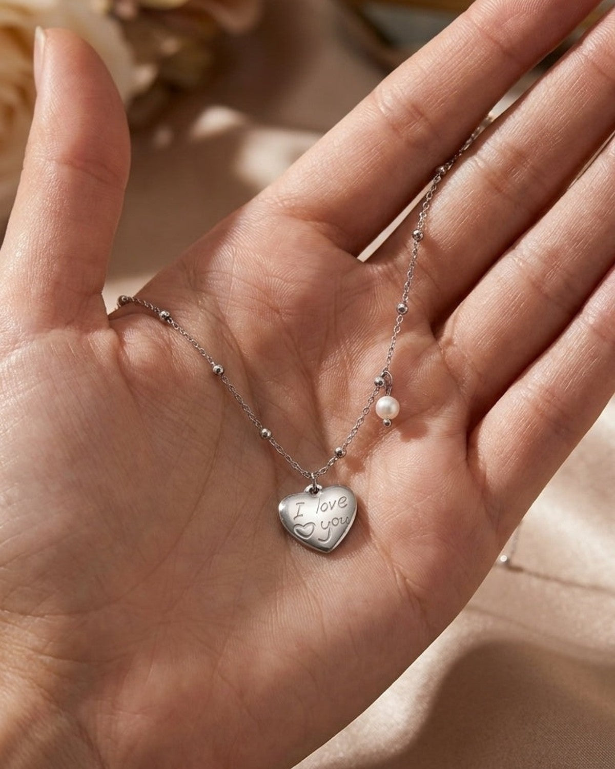 Silver Dripping Pearl Heart necklace with an engraved "I love you" pendant rests in an open palm.