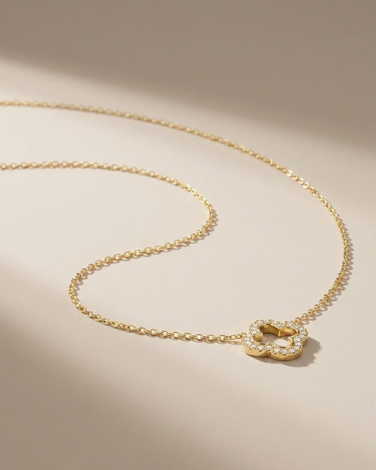 Gold clover pendant necklace with dainty chain and a delicate pavé diamond-style inlay on a neutral background.