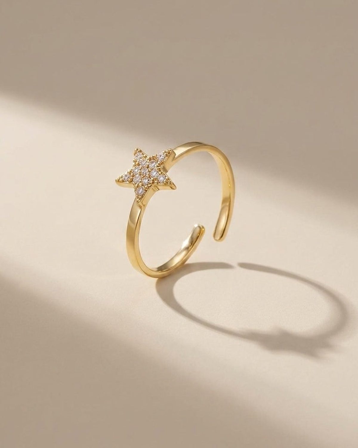 A gold open ring featuring a paved gemstone star on a beige surface.