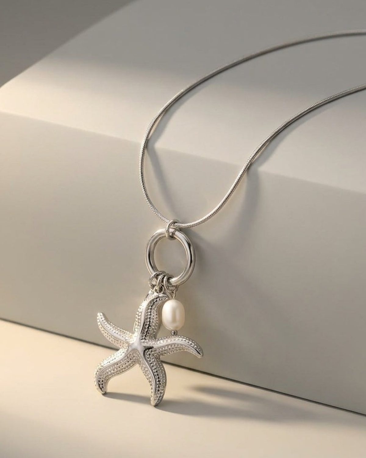 Silver pendant necklace featuring a textured starfish and a small white pearl hanging from a ring bail.