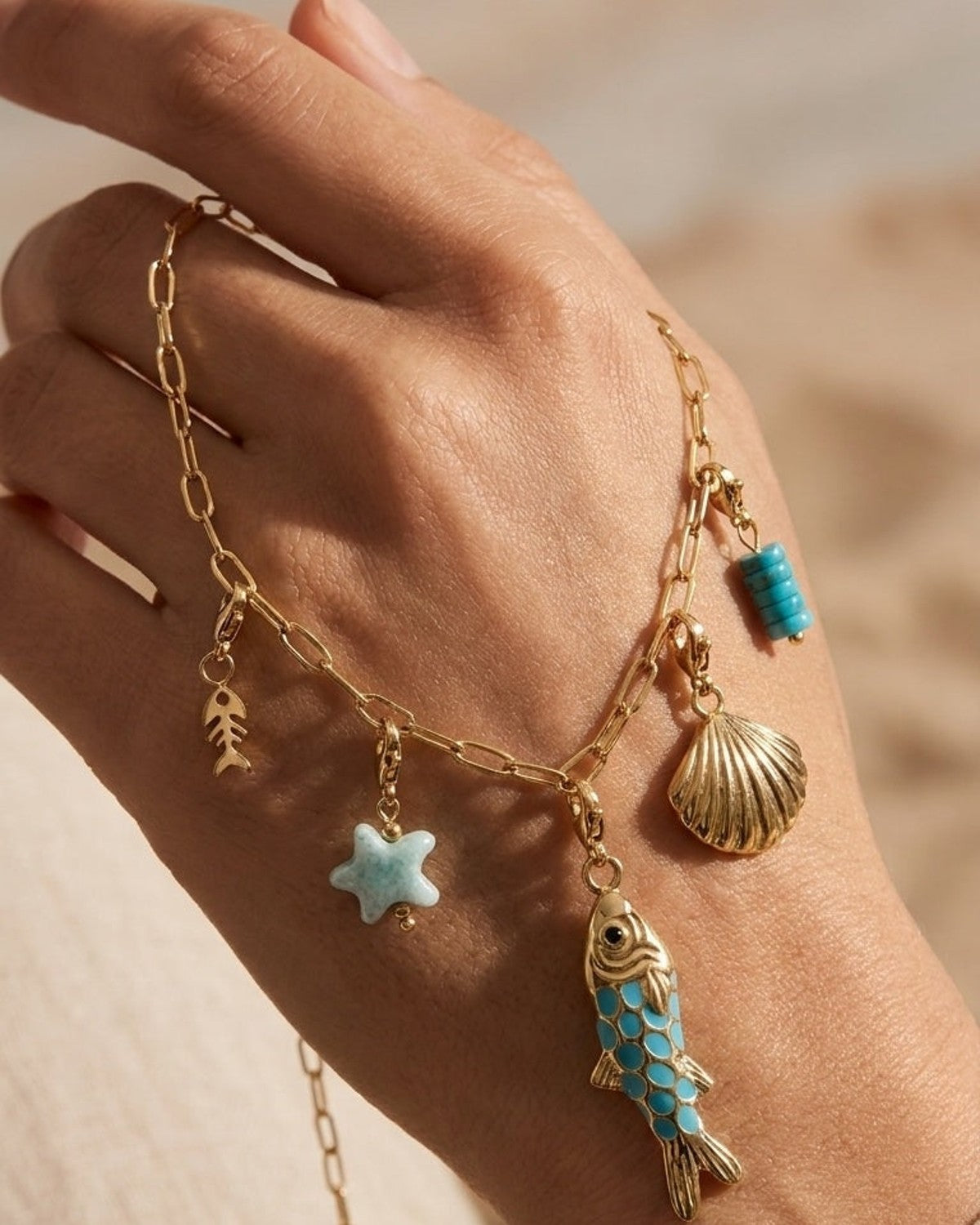 Gold link necklace with ocean charms: fishbone, blue starfish, fish, shell, and bead.