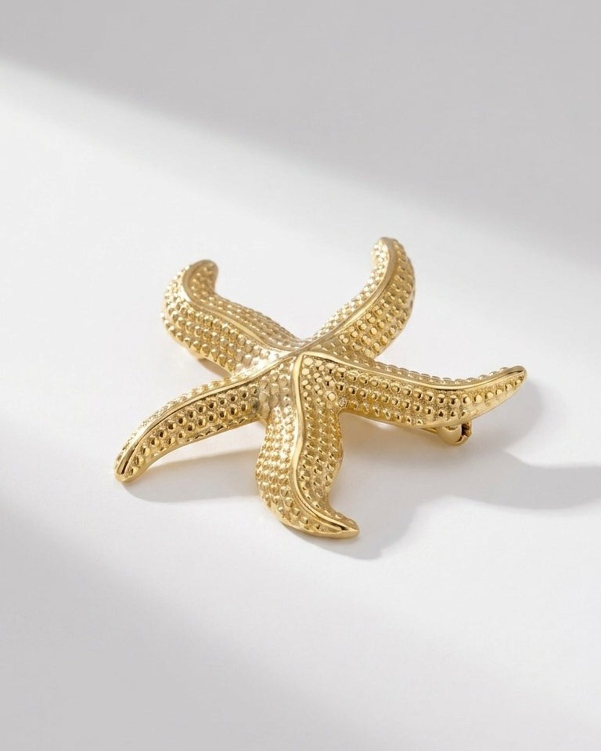Gold starfish brooch with textured, pebbled details on a white background.