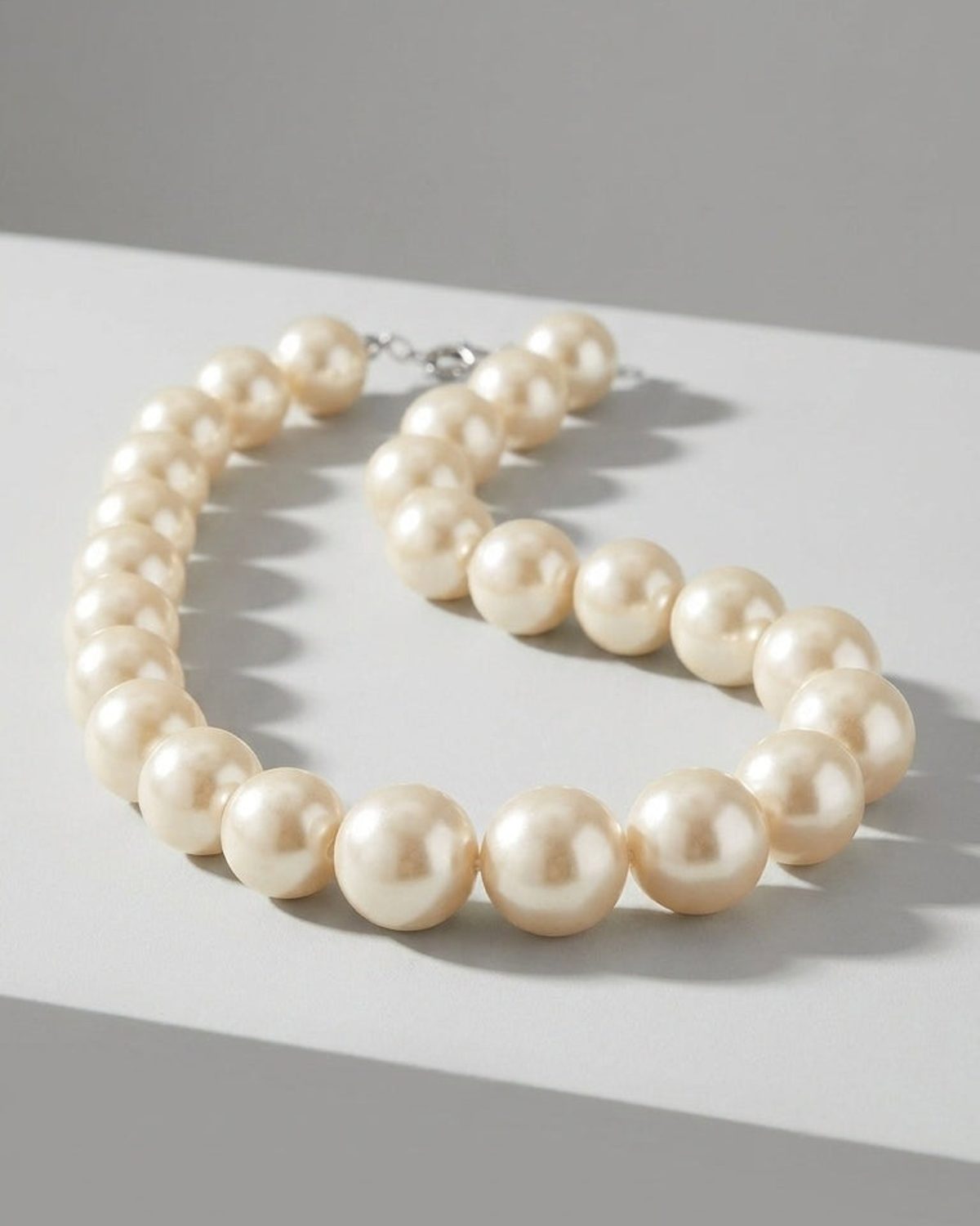 A chunky pearl necklace with large, cream-colored beads resting on a light gray surface.