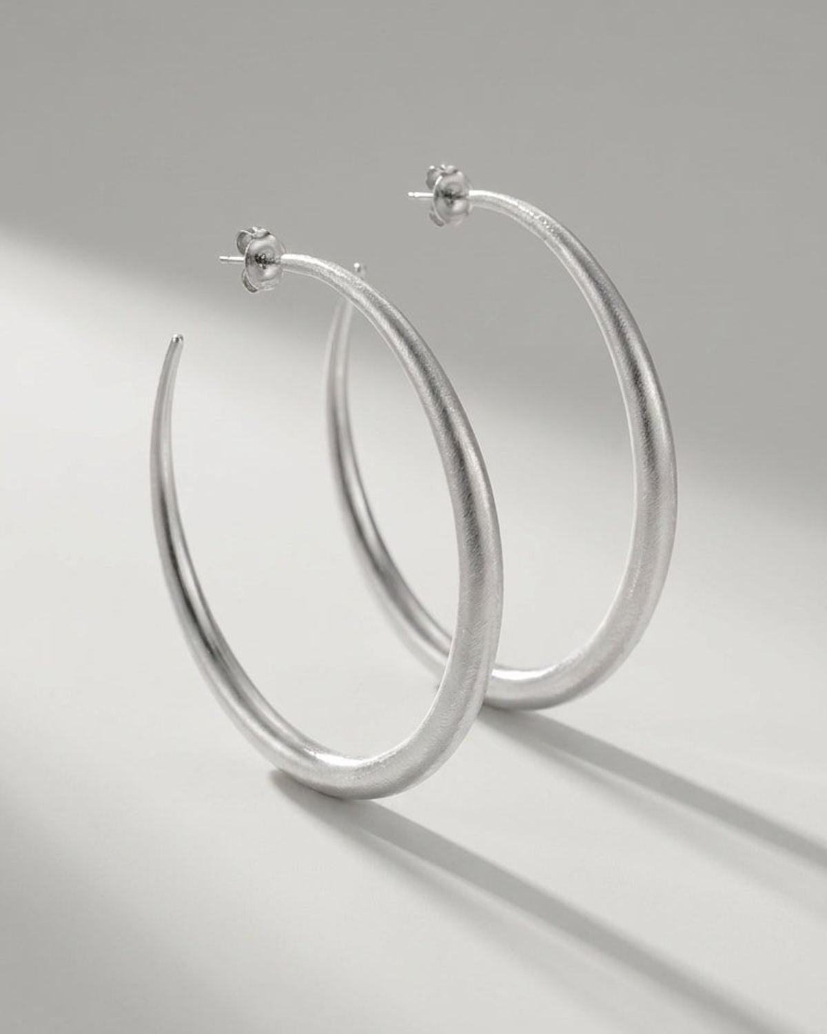 Aura Melt Gold hoop earrings in silver, featuring a sleek, minimalist style with a textured, matte finish.
