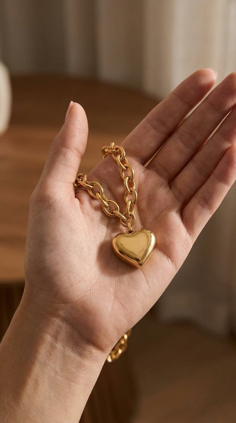 Gold heart pendant necklace with a polished, puffy heart charm on a textured cable chain, held in a person's palm.
