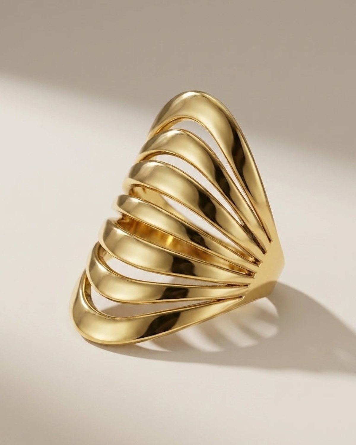 Bold, polished gold-tone ring featuring a dramatic, tiered cage-like design with overlapping arches.