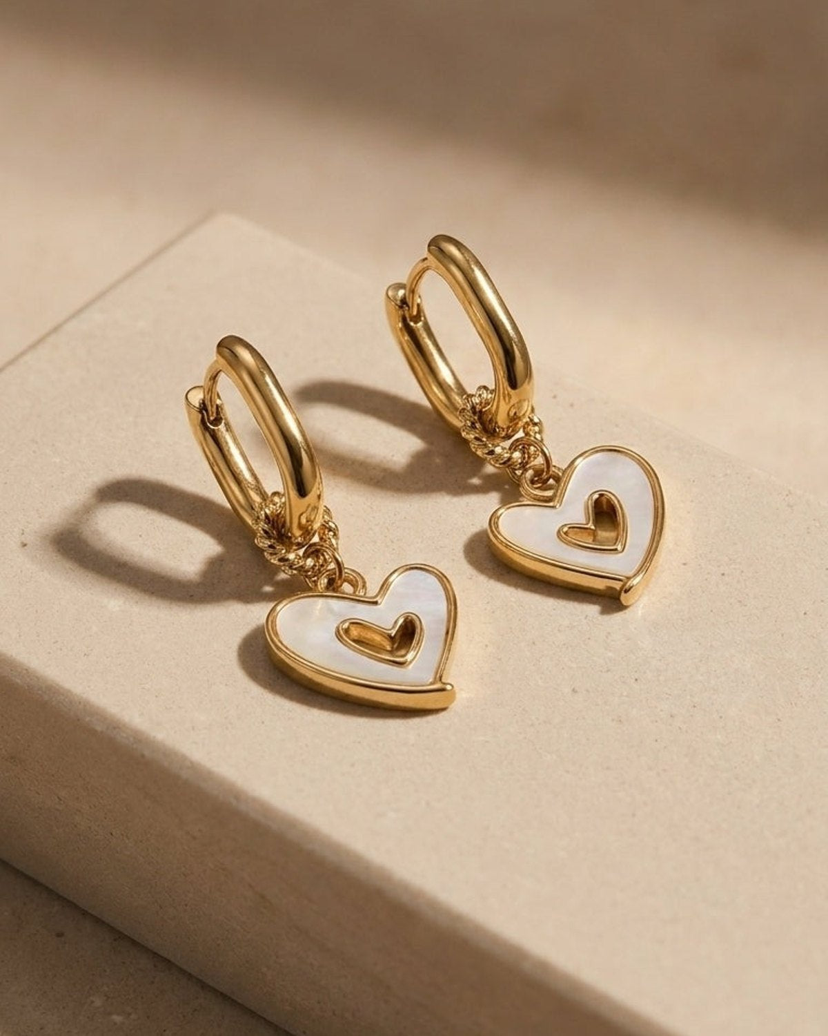 Gold hoop earrings with dangling heart charms inlaid with white mother-of-pearl and a raised gold inner heart.