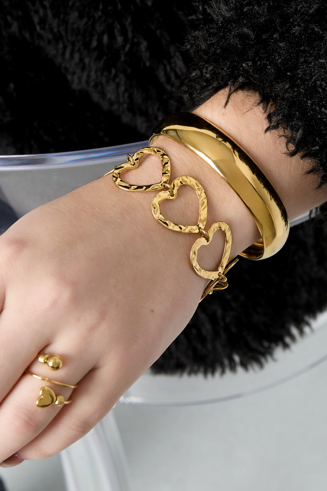 Woman's wrist wearing stacked bracelets including the hammered heart link bracelet in gold-tone metal and a smooth gold bangle