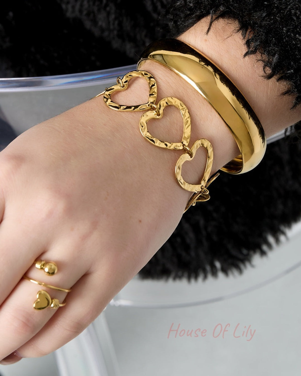 Woman's wrist wearing stacked bracelets including the hammered heart link bracelet in gold-tone metal and a smooth gold bangle