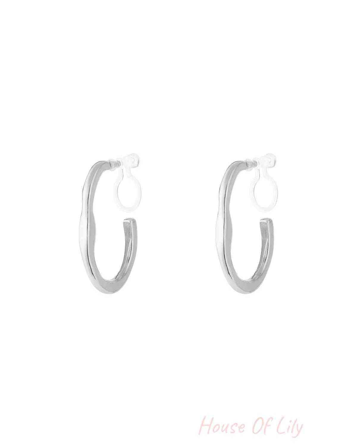 Pair of silver irregular wave-shaped clip-on hoop earrings with clear clip backs on white background