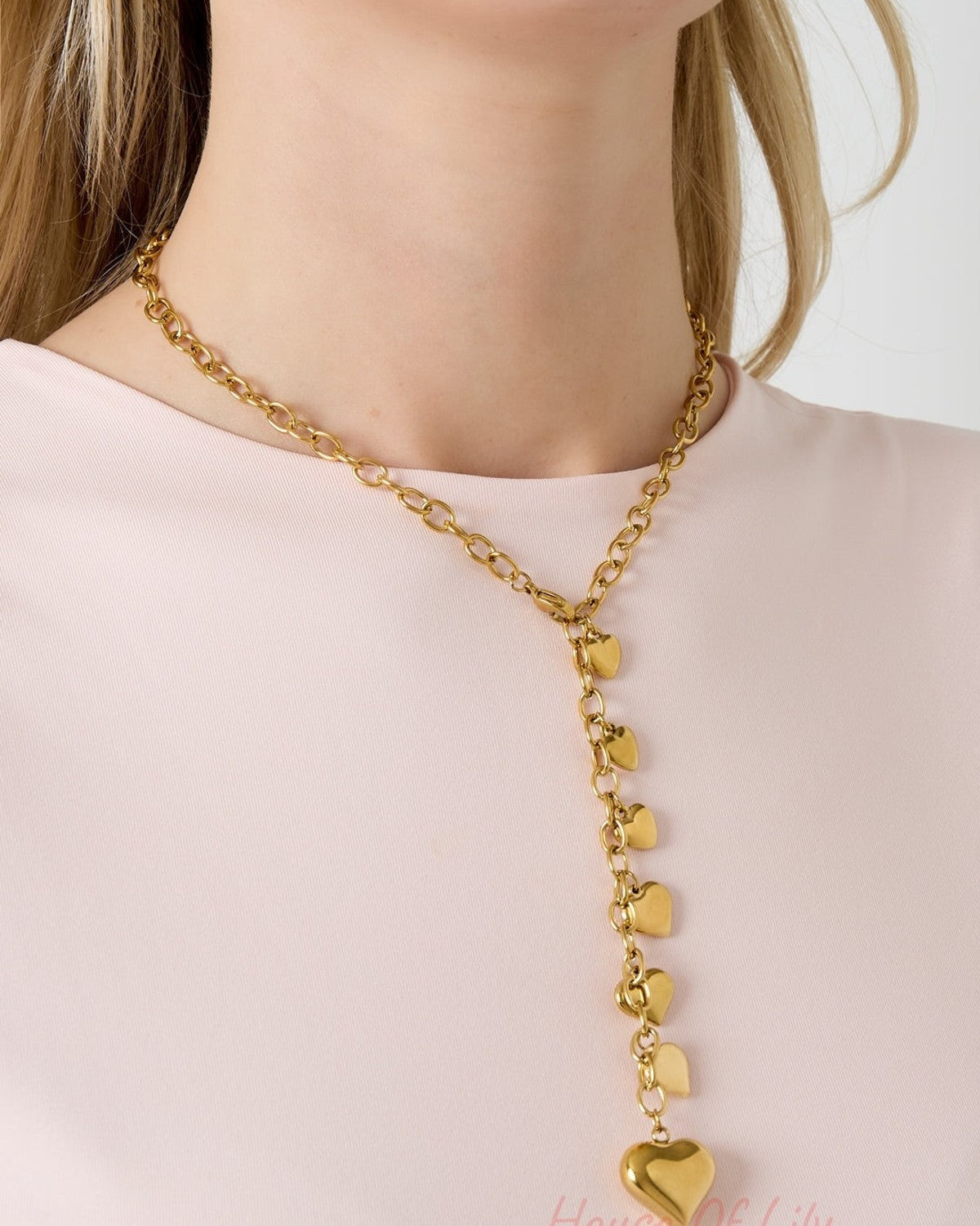 Model wearing a gold-tone heart charm necklace with cascading hearts, styled with a light pink top